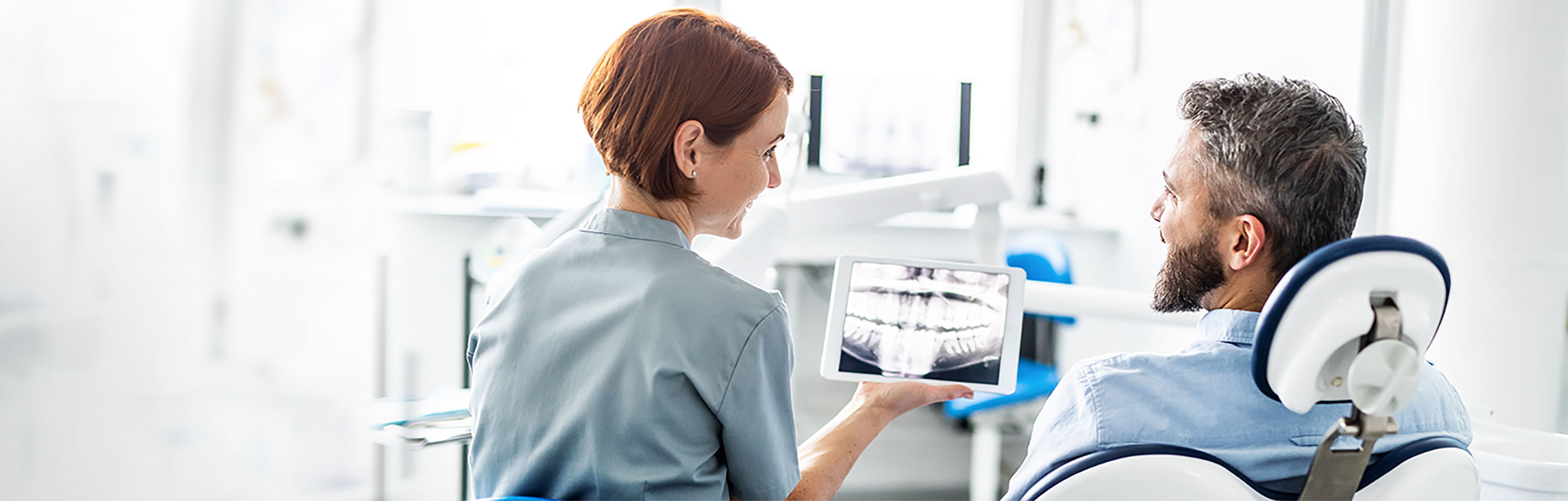 A dental care professional shows a patient an x-ray on a computer tablet