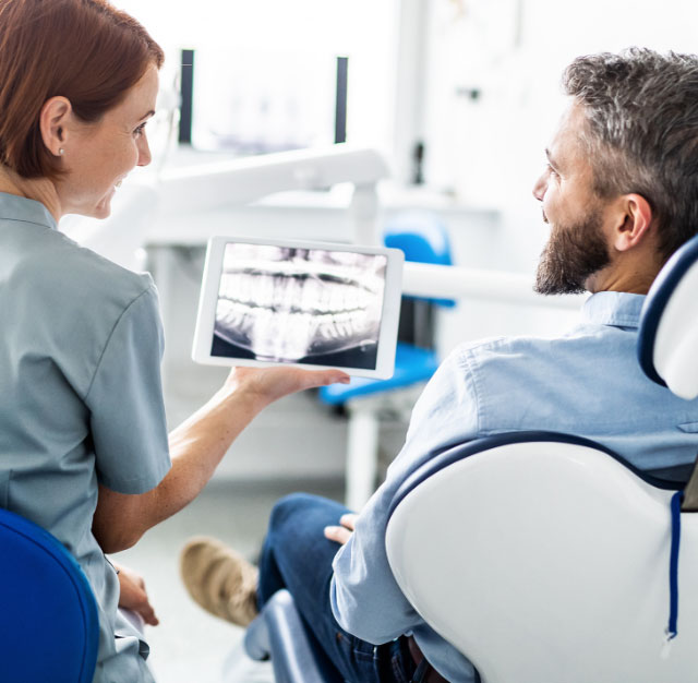 A dental care professional shows a patient an x-ray on a computer tablet