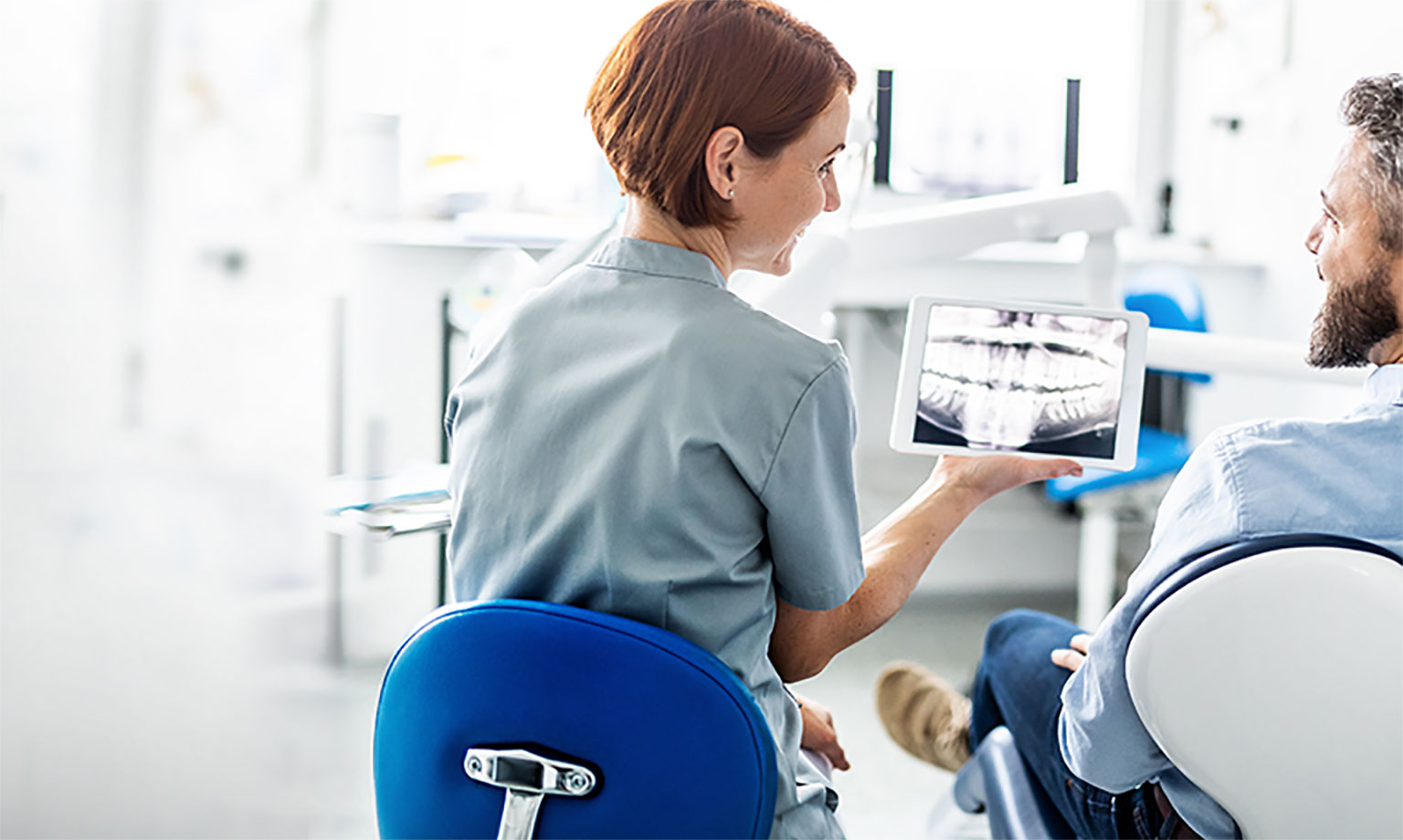 A dental care professional shows a patient an x-ray on a computer tablet
